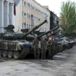 Luhansk People's Republic people militia servicemen stand at an exhibition of captured Ukrainian tanks and weapons in Lisichansk, on the territory which is under the Government of the control, eastern Ukraine, Tuesday, July 12, 2022. The West's move to send tanks to Ukraine was greeted enthusiastically from Kyiv, Berlin and Washington. But Moscow seemed to shrug. The Kremlin has warned the West that supplying tanks would be a dangerous escalation of the conflict and denounced the decision.