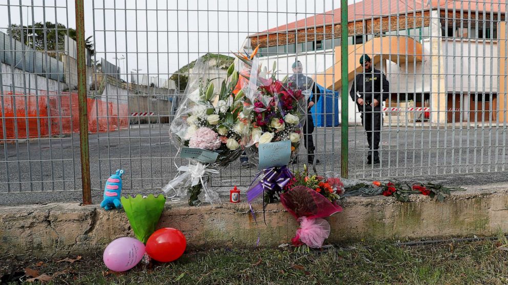Members of the Guardia di Finanza stand next to floral tributes laid at the fence of PalaMilone sports hall, where victims of a deadly migrant shipwreck are being held, in Crotone, Italy, Feb. 27, 2023.