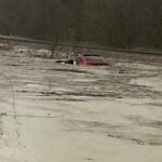 In this photo provided by Layton Hoyer, a red SUV is seen submerged in floodwater on Old Ritchey Road in Granby, Mo., early Friday, March 24, 2023. Hoyer rescued an elderly woman from the car. (Layton Hoyer via AP)